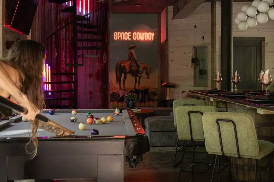Guest playing pool beside the bar under a Space Cowboy neon sign