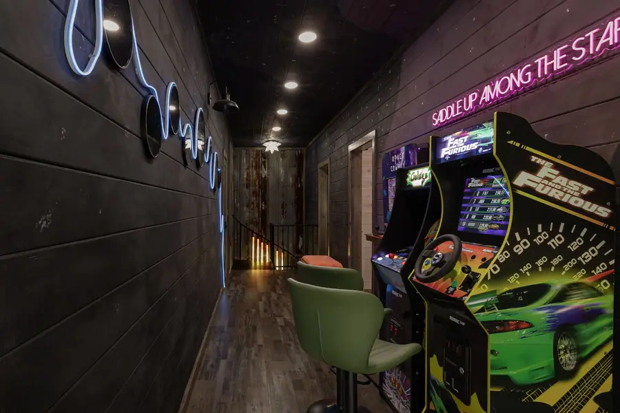 Arcade hallway with neon 'saddle up among the stars' sign and racing arcade cabinets